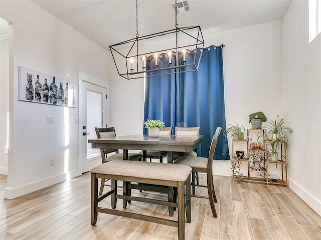 dining space with visible vents, light wood finished floors, baseboards, and a notable chandelier