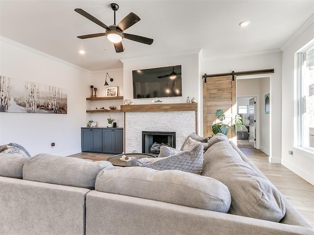 living room with crown molding, ceiling fan, a barn door, baseboards, and light wood-type flooring
