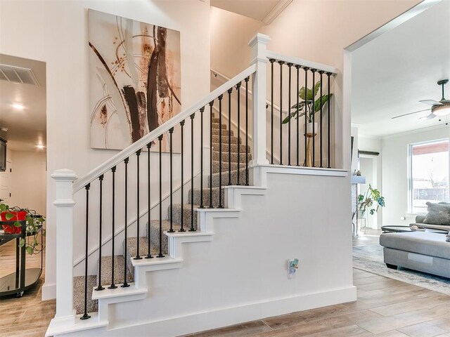 stairway with ceiling fan, visible vents, ornamental molding, and wood finished floors