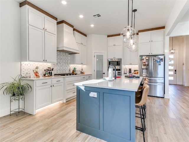 kitchen featuring light wood-style floors, custom exhaust hood, stainless steel appliances, and visible vents