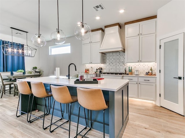 kitchen featuring a kitchen island with sink, visible vents, premium range hood, and light wood-style floors