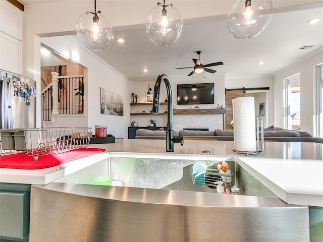 kitchen with a sink, a ceiling fan, open floor plan, visible vents, and ornamental molding