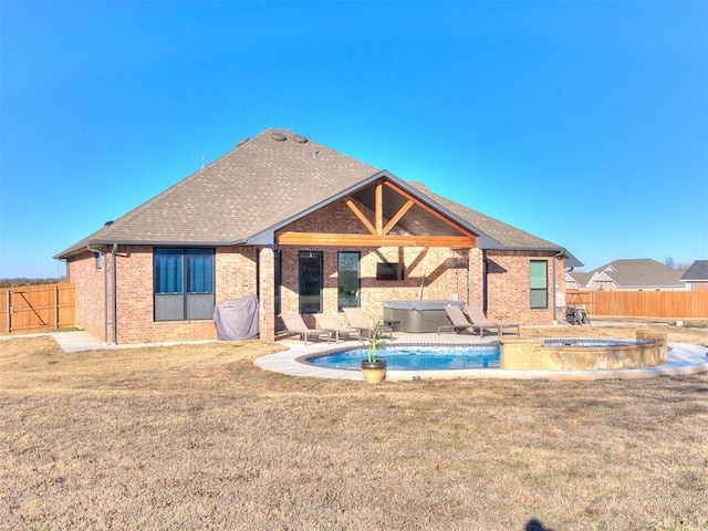 back of house featuring a shingled roof, a hot tub, brick siding, a fenced backyard, and a yard