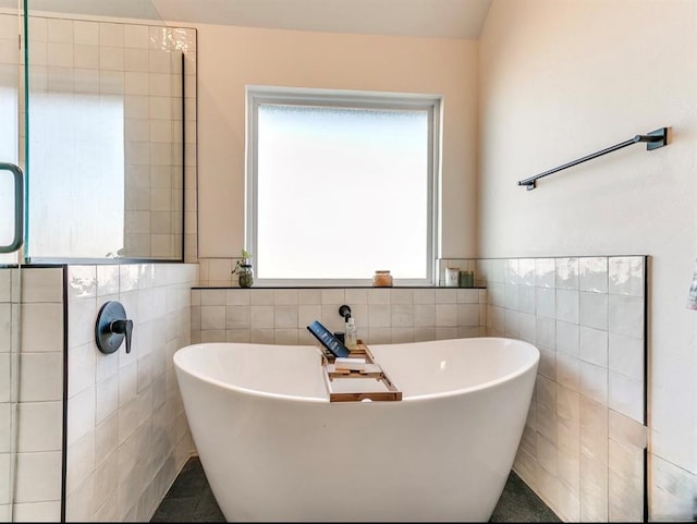 full bathroom featuring a healthy amount of sunlight, tile walls, and a soaking tub