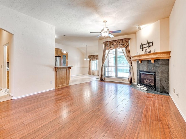 unfurnished living room featuring a textured ceiling, arched walkways, a tile fireplace, a ceiling fan, and light wood finished floors