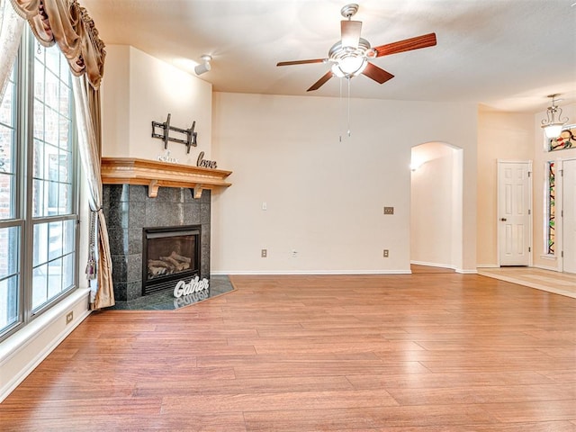 unfurnished living room with ceiling fan, arched walkways, a fireplace, wood finished floors, and baseboards