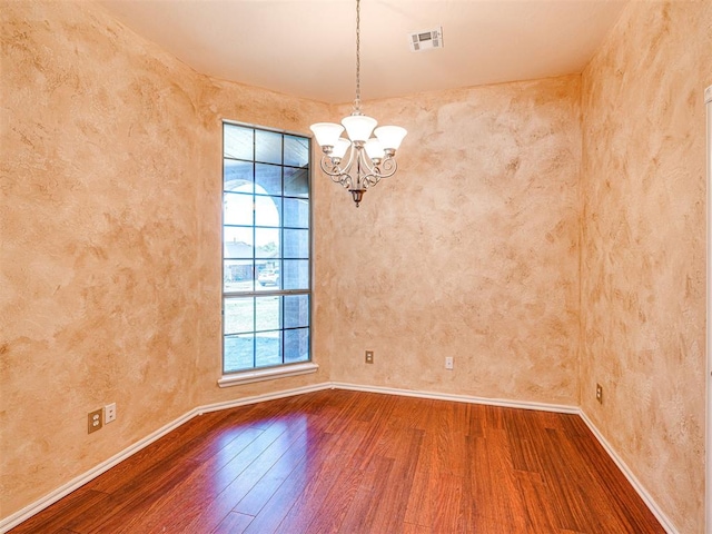 unfurnished room featuring baseboards, a notable chandelier, wood finished floors, and visible vents
