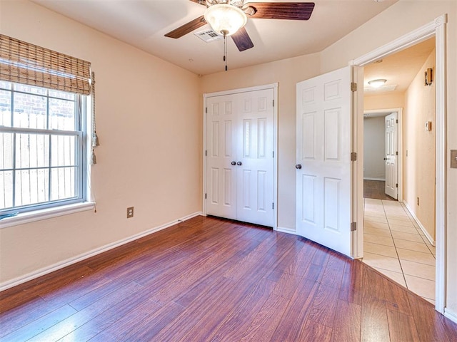 unfurnished bedroom featuring a closet, visible vents, wood finished floors, baseboards, and ceiling fan