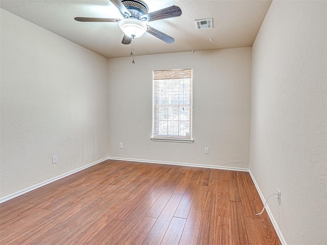 spare room featuring visible vents, a textured wall, wood finished floors, baseboards, and ceiling fan