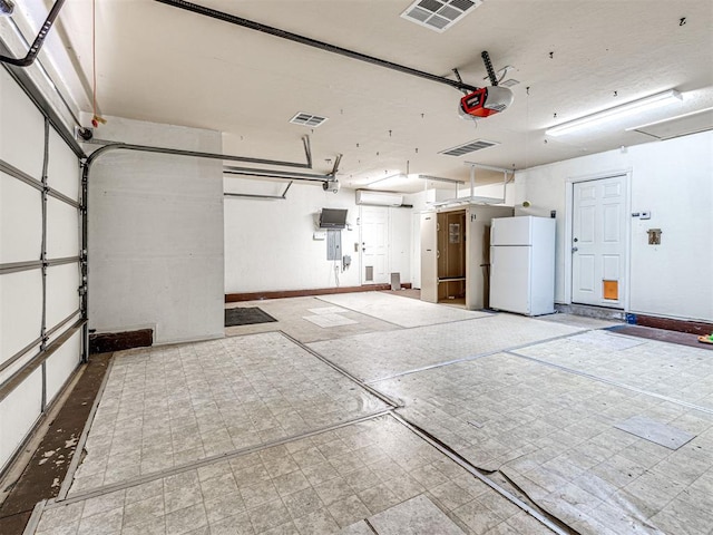 garage featuring visible vents, freestanding refrigerator, a garage door opener, and baseboards