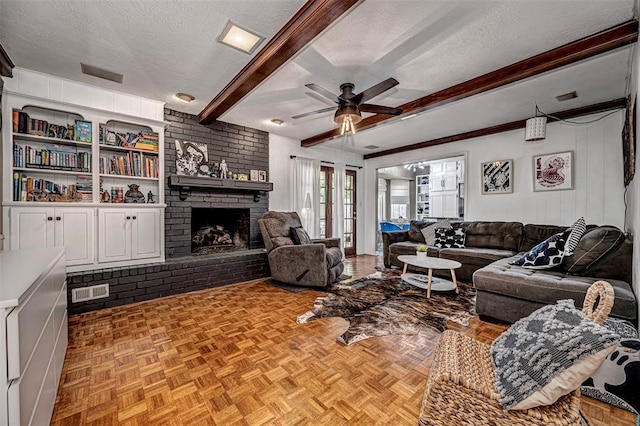 living area with beamed ceiling, a ceiling fan, a textured ceiling, and a fireplace