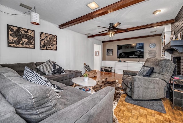 living room with a textured ceiling, beam ceiling, a ceiling fan, and a brick fireplace