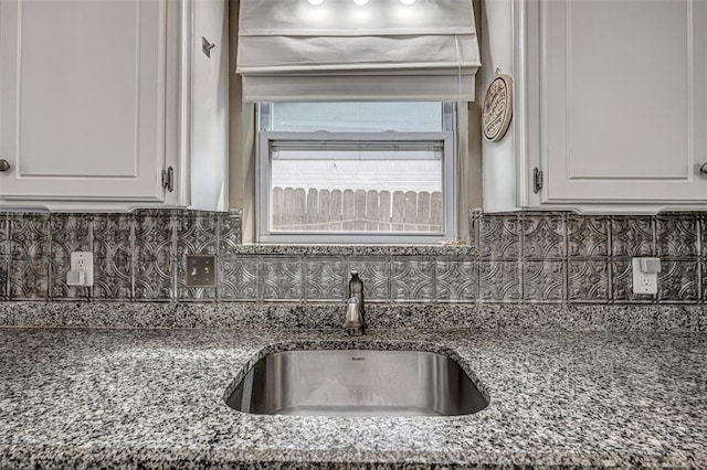 kitchen with a sink, decorative backsplash, white cabinets, and stone countertops