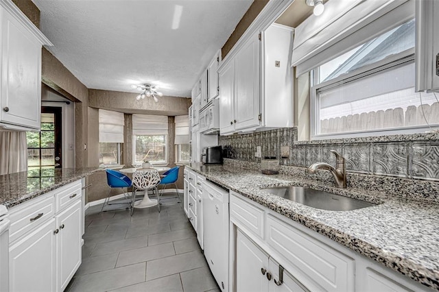 kitchen with white dishwasher, white cabinetry, light tile patterned floors, and a sink