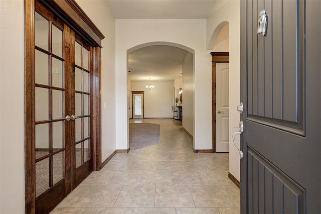 hall with arched walkways, french doors, and baseboards