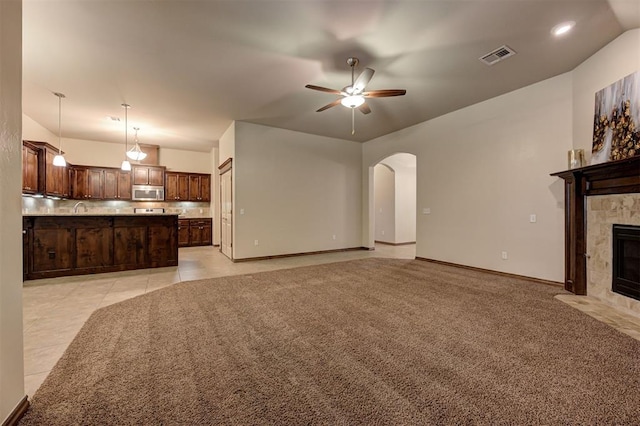 unfurnished living room featuring a tiled fireplace, arched walkways, ceiling fan, baseboards, and visible vents