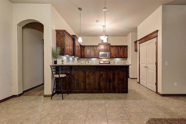 kitchen with stainless steel microwave, tasteful backsplash, visible vents, a peninsula, and dark brown cabinets