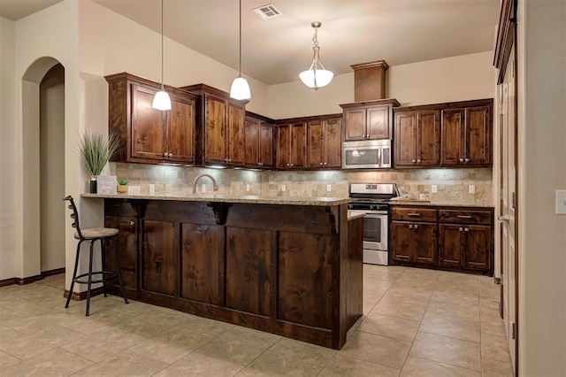 kitchen with a breakfast bar area, a peninsula, appliances with stainless steel finishes, and light stone counters