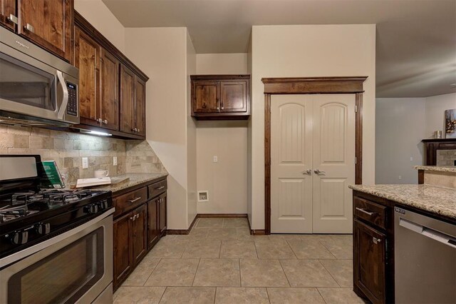 kitchen featuring backsplash, light stone countertops, dark brown cabinetry, and appliances with stainless steel finishes