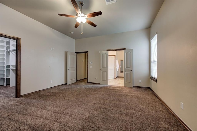 unfurnished bedroom with visible vents, baseboards, light carpet, a spacious closet, and a ceiling fan