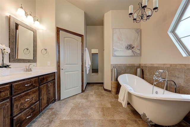 full bathroom with stone finish flooring, a freestanding bath, a notable chandelier, and vanity
