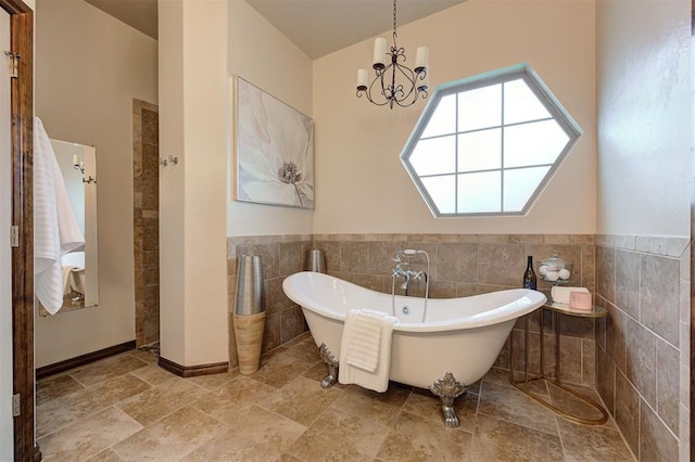 bathroom featuring tile walls, an inviting chandelier, wainscoting, and a soaking tub