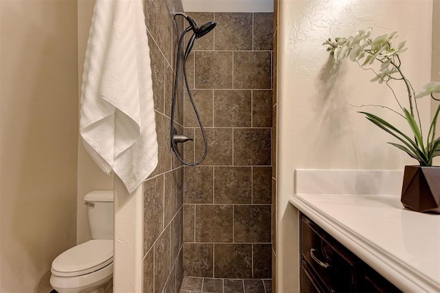 full bathroom with tiled shower, toilet, and vanity