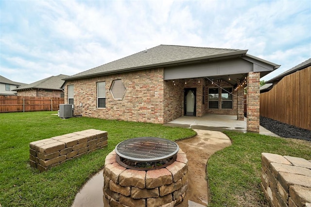 back of property with a patio area, a fenced backyard, a lawn, brick siding, and a fire pit