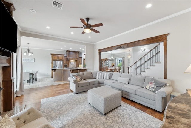532 Conquistador Ct, Edmond, OK 73025 - living room featuring stairway, light wood-type flooring, crown molding, visible vents, and ceiling fan with notable chandelier