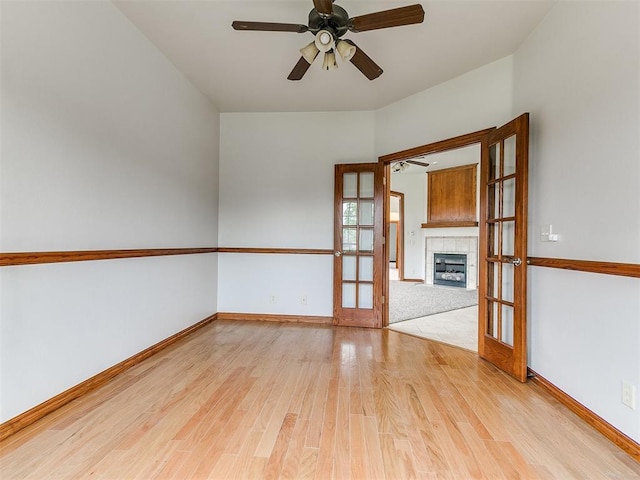 spare room with a fireplace, ceiling fan, french doors, and light wood-type flooring