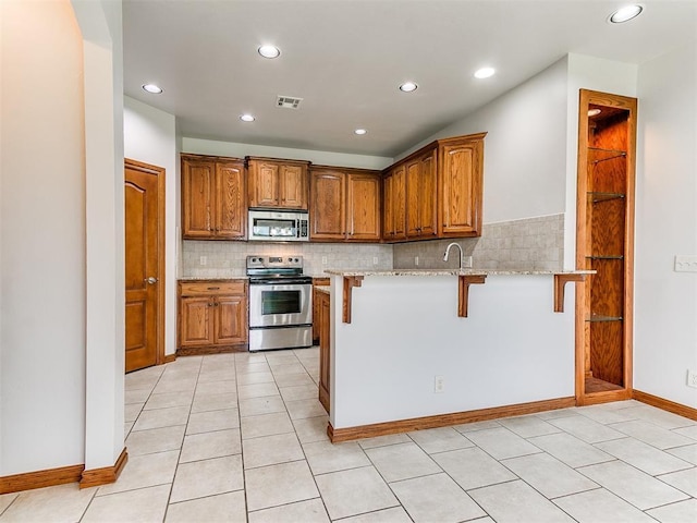 kitchen with light stone countertops, appliances with stainless steel finishes, a breakfast bar, backsplash, and visible vents