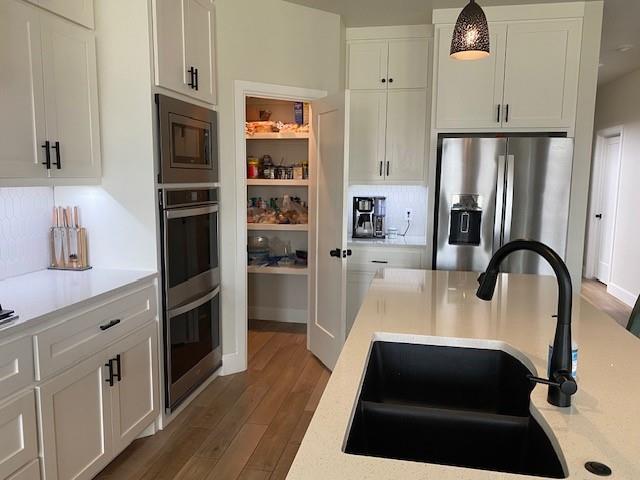 kitchen featuring wood finished floors, stainless steel appliances, light countertops, white cabinets, and a sink