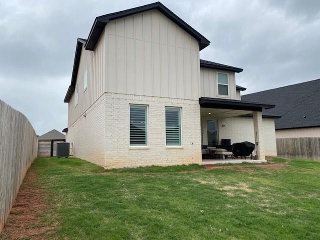 rear view of property featuring board and batten siding, a patio area, brick siding, and a fenced backyard