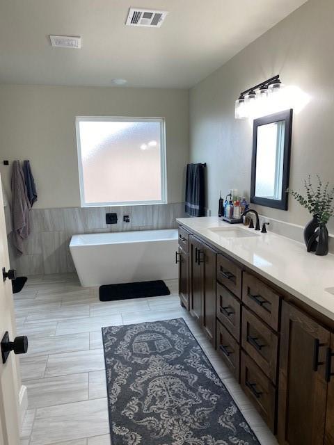 full bath featuring a soaking tub, visible vents, double vanity, and a sink