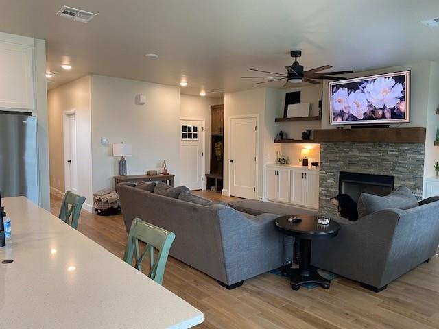 living room with recessed lighting, light wood-style floors, a stone fireplace, visible vents, and a ceiling fan