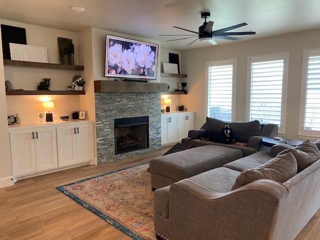 living area featuring a ceiling fan, light wood-style floors, and a fireplace