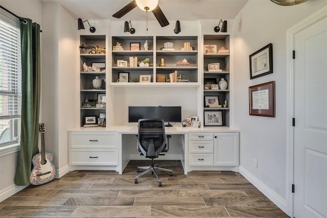 office area featuring baseboards, ceiling fan, wood finish floors, and built in desk