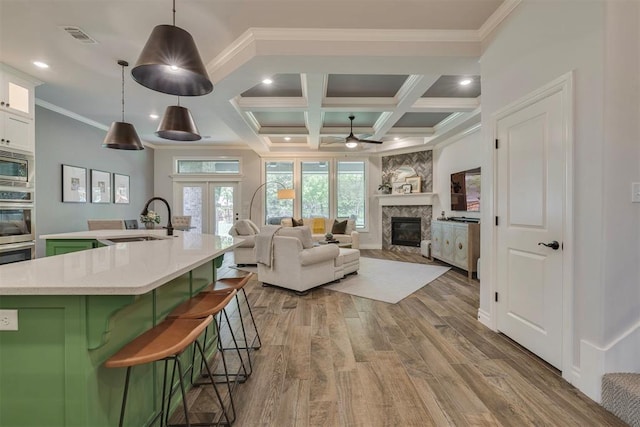 living area featuring crown molding, visible vents, a glass covered fireplace, wood finished floors, and ceiling fan