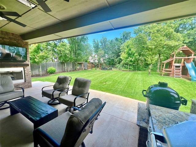 8817 Arya Rd, Edmond, OK 73007 - fenced backyard featuring a patio, ceiling fan, a playground, view of wooded area, and an outdoor living space with a fireplace