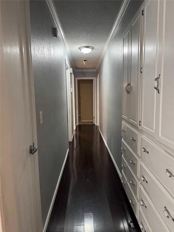 hallway with dark wood-type flooring, baseboards, a textured ceiling, and crown molding
