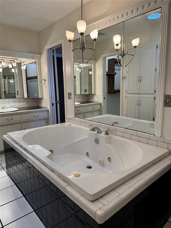 bathroom featuring a whirlpool tub, vanity, tile patterned flooring, and a chandelier