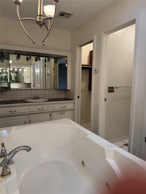 bathroom with a tub with jets, vanity, visible vents, a notable chandelier, and a textured ceiling