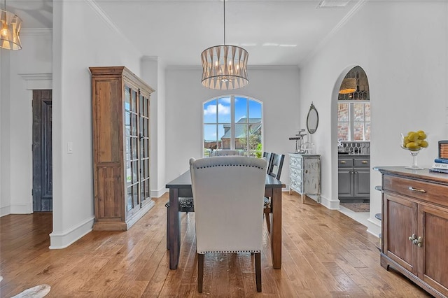 dining area with baseboards, ornamental molding, light wood finished floors, and a chandelier