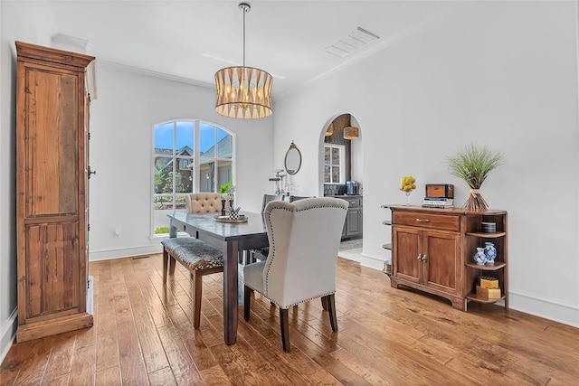 dining space featuring baseboards, ornamental molding, light wood-style flooring, and arched walkways