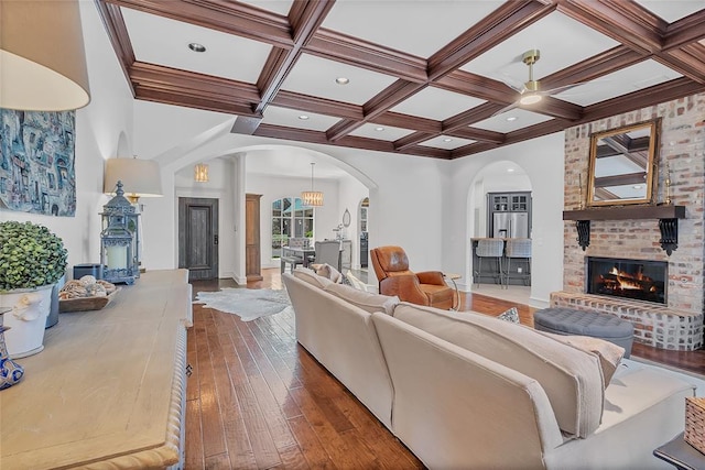 living room featuring arched walkways, coffered ceiling, a brick fireplace, and hardwood / wood-style flooring