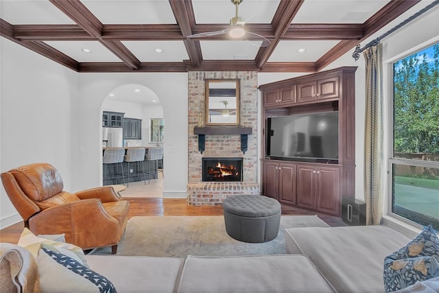 living area featuring coffered ceiling, a ceiling fan, light wood finished floors, and beam ceiling