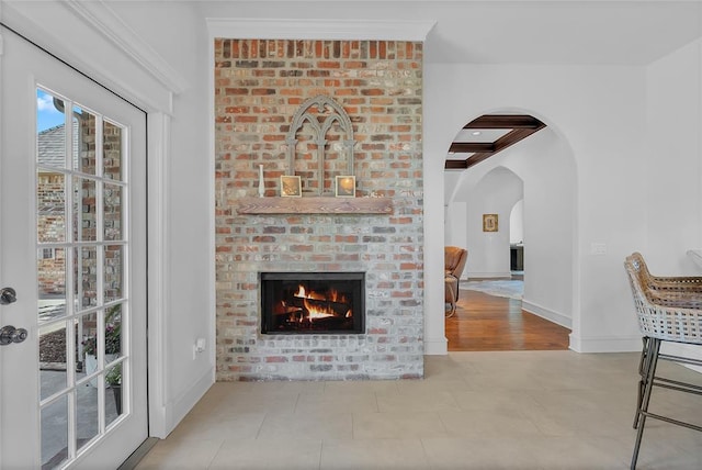 living room with arched walkways, a brick fireplace, beam ceiling, baseboards, and coffered ceiling