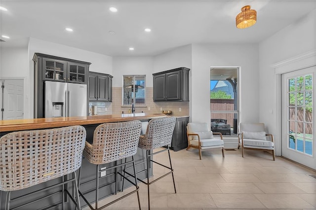 kitchen with glass insert cabinets, decorative backsplash, a breakfast bar area, stainless steel fridge, and recessed lighting