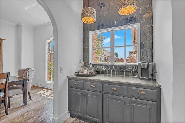 bar with crown molding, arched walkways, wood finished floors, baseboards, and a bar