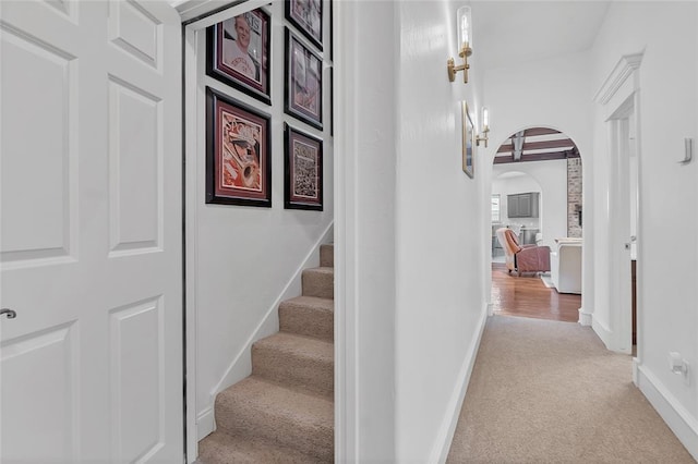 corridor featuring carpet flooring, arched walkways, baseboards, and stairs